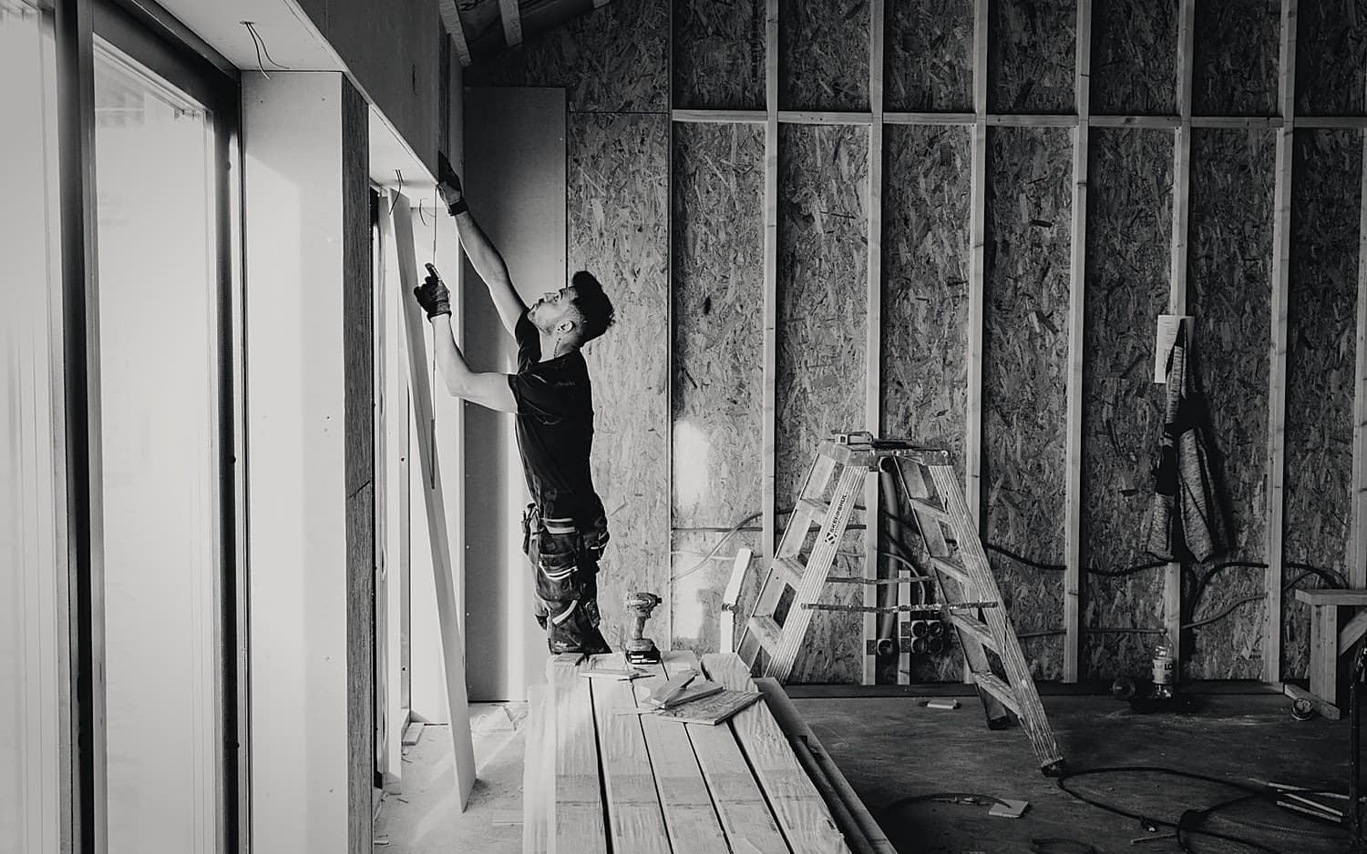 A drywall installer fixing boards to a wood-framed wall on a job site